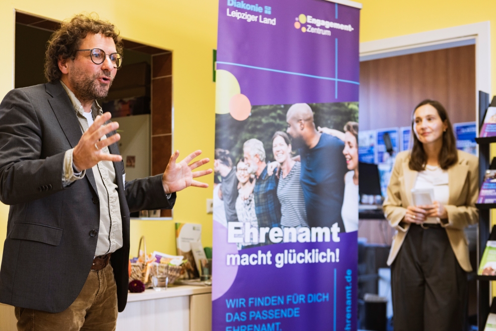 Während der Begrüßung der Ergebnisse steht der Fachbereichsleiter Herr Jahn links und die Einrichtungsleitung des Engagement-Zentrum Frau Franke rechts vor einem BAnner mit der Aufschrift " Ehrenamt macht glücklich".