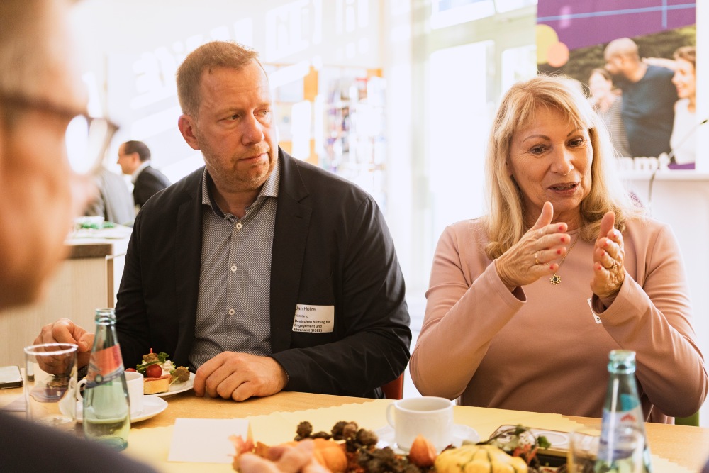 Die sächsische Sozialministerin Petra Köpping und Jan Holze, Vorstand der Deutschen Stiftung für Engagement und Ehrenamt (DSEE), sitzen an einem Tisch und tauschen sich mit weiteren Anwesenden aus.
